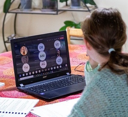 woman in front of a laptop with a teams meeting showing on it on a kitchen table at home